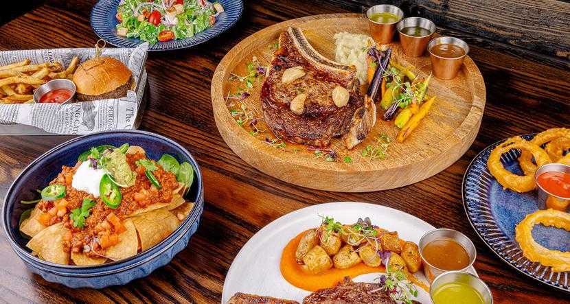 Table spread of nachos, steaks, onion rings and a burger